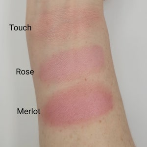 May include: Swatch of three blush colors on a person's arm. The colors are labeled "Touch", "Rose", and "Merlot".