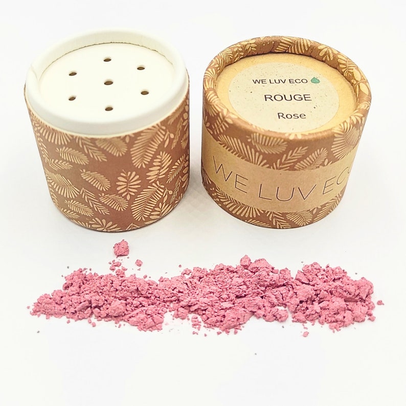 May include: Two cardboard containers with a leaf pattern and the text "WE LUV ECO" and "ROUGE Rose" on the label. A pink powder is spilled out of the container.