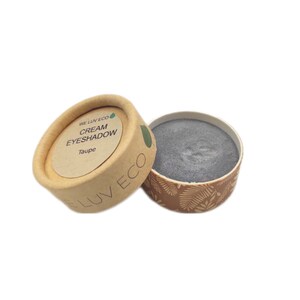May include: A small, round container of cream eyeshadow in the color taupe. The container is made of cardboard and has a brown and white design. The label on the container reads "We Luv Eco Cream Eyeshadow Taupe".