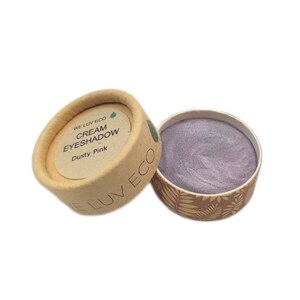 May include: A small, round container of dusty pink cream eyeshadow. The container is made of cardboard and has a green leaf logo with the text "WE LUV ECO" and "CREAM EYESHADOW" printed on it.