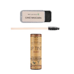 Könnte beinhalten: Ein Set veganer und biologischer Make-up-Produkte. Eine braune Tube mit dem Text "Lip Tint Nude" und "We Luv Eco" mit einem grünen Blattlogo. Eine kleine silberne Dose mit dem Text "Cake Mascara" und "We Luv Eco". Ein Holzstab mit einer schwarzen Mascara-Bürste.