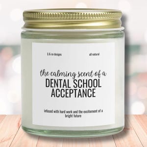 Puede incluir: Un tarro de vidrio para velas con tapa dorada. La etiqueta dice "the calming scent of a DENTAL SCHOOL ACCEPTANCE infused with hard work and the excitement of a bright future".