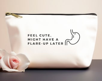 Pode incluir: Bolsa de maquilhagem de lona branca com fecho de correr preto e guarnição preta. A bolsa tem um desenho de linha preta de um estômago com o texto "Feel cute, might have a flare-up later".