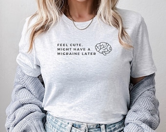 Puede incluir: Camiseta gris claro con el texto "FEEL CUTE, MIGHT HAVE A MIGRAINE LATER" y un gráfico de cerebro. La camiseta es de cuello redondo y está hecha de un material suave. Es una prenda de vestir informal.