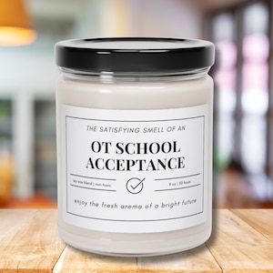 May include: A white candle jar with a black lid and a white label that reads "THE SATISFYING SMELL OF AN OT SCHOOL ACCEPTANCE soy wax blend | non-toxic 9 oz | 50 hours enjoy the fresh aroma of a bright future".