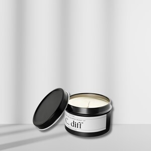 May include: A black metal candle tin with a white label that reads "The most calming scent of C. diff". The lid is off and the candle is partially lit.