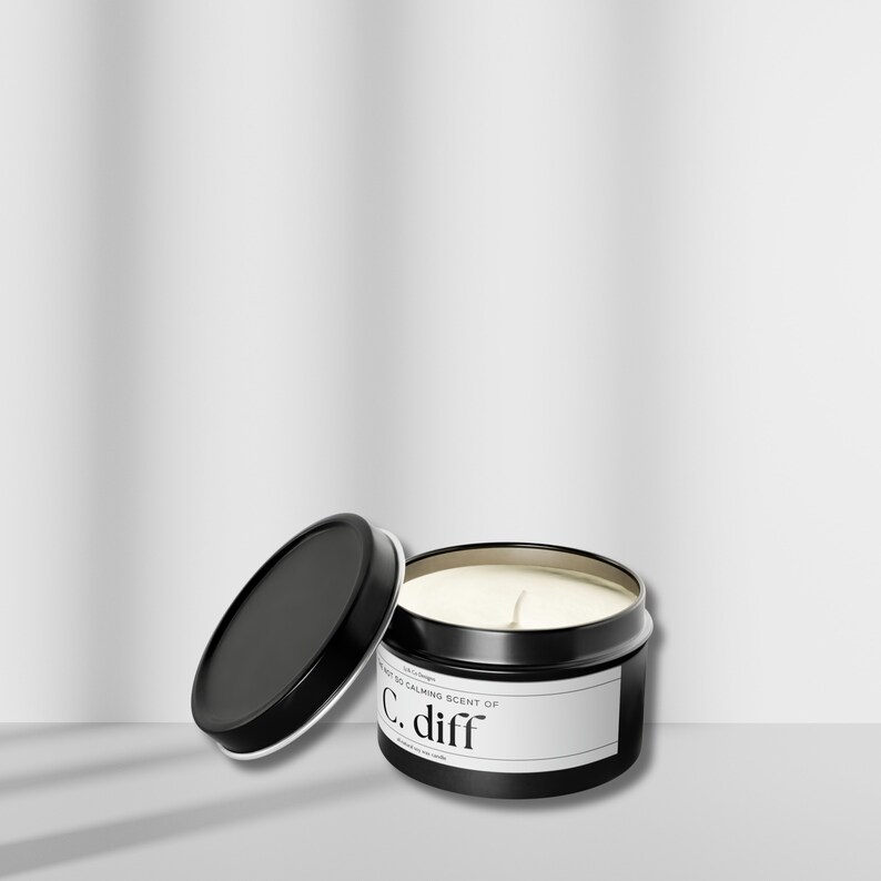 May include: A black metal candle tin with a white label that reads "The most calming scent of C. diff". The lid is off and the candle is partially lit.