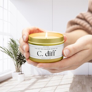 May include: A gold candle tin with a white label that reads "The not so calming scent of C. diff all natural soy wax candle".