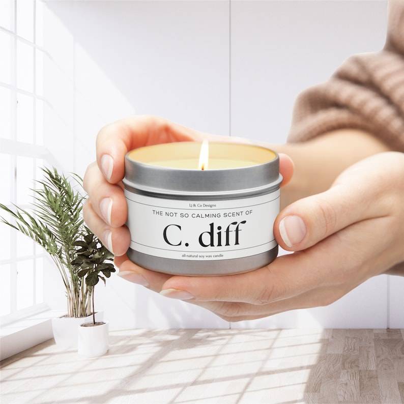 May include: A silver candle tin with a white label that reads "The not so calming scent of C. diff all natural soy wax candle".