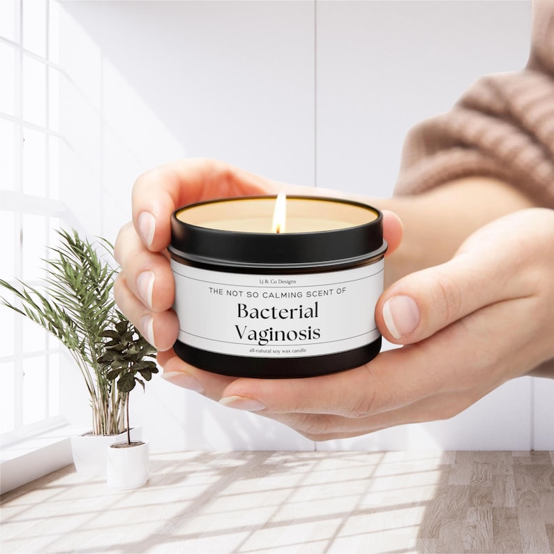 May include: A black candle tin with a white label that reads "The Not So Calming Scent of Bacterial Vaginosis, all natural soy wax candle".