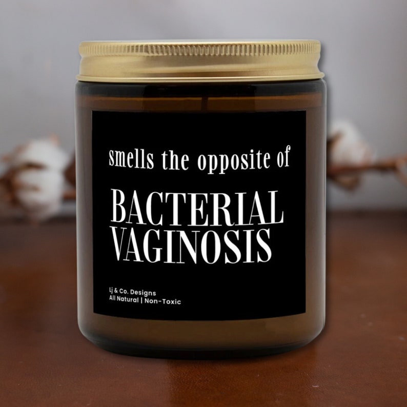 May include: A brown glass candle with a gold lid and a black label that reads "smells the opposite of BACTERIAL VAGINOSIS" and "Lj & Co. Designs All Natural | Non-Toxic".