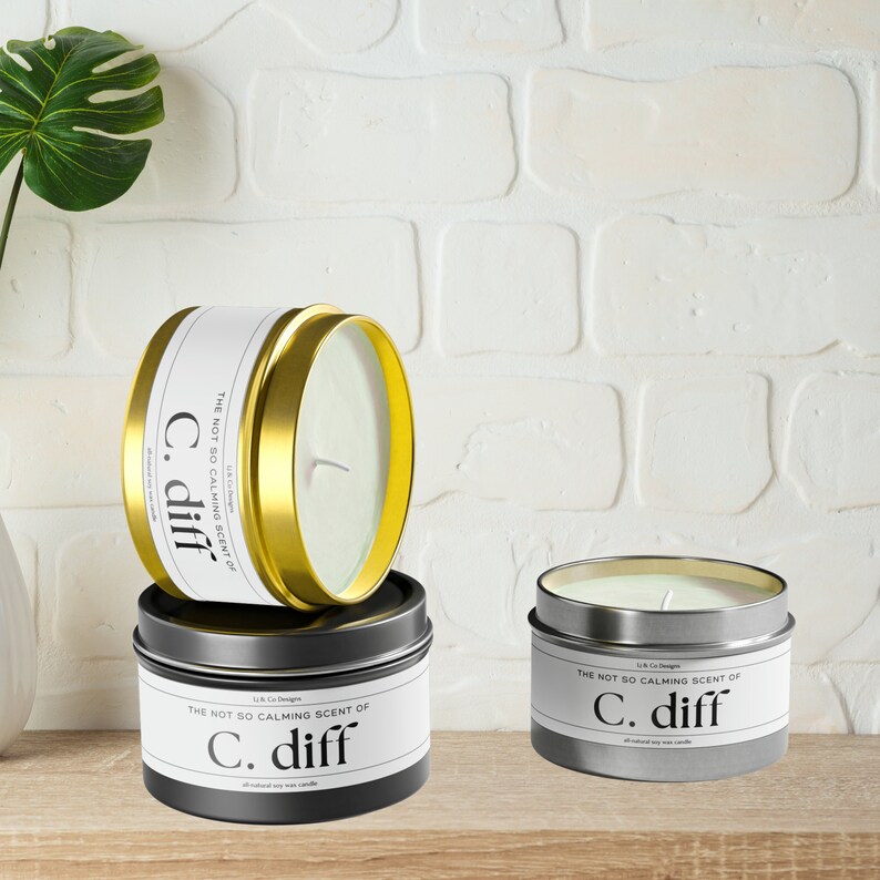 May include: Three candles in different colored tins. The candles are labeled "The Not So Calming Scent of C. diff." The candles are all natural soy wax candles.