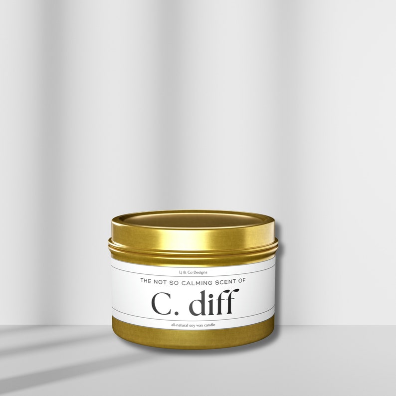 May include: Gold metal candle tin with a white label that reads "The not so calming scent of C. diff all-natural soy wax candle".