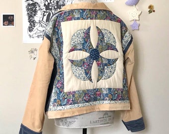 May include: A tan corduroy jacket with a quilted back panel. The quilted panel is made of white fabric with a blue and white floral print. The jacket has a blue denim collar and cuffs.