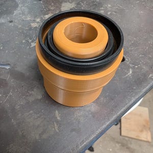 Op de afbeelding: Een 3D-geprint object met een cilindrisch ontwerp. Het object bestaat uit concentrische ringen in tinten bruin en zwart. De bruine secties hebben een matte afwerking, terwijl de zwarte ring glad lijkt. Het object staat op een metalen oppervlak.