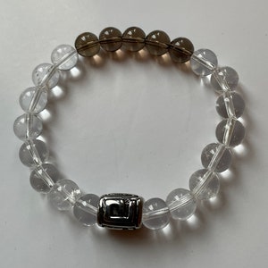 May include: A bracelet made with clear and smoky quartz beads with a silver charm in the centre.