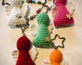 May include: Five crocheted angel keychains with white wings and star-shaped buttons. The angels are in different colors: white, pink, green, red, and orange. The keychains are connected by a silver chain with star-shaped charms.