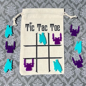May include: A canvas Tic Tac Toe game set with a drawstring bag. The bag has the game title printed on it. The game pieces are teal and purple.