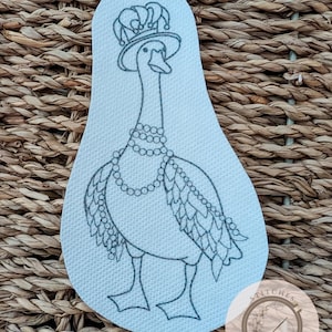 Puede incluir: Un parche de color claro con un ganso de dibujos animados que lleva una corona, un sombrero y un collar de perlas. El ganso tiene diseños de plumas detallados y está de pie. El parche está sobre un fondo tejido, con un logotipo circular en la esquina inferior derecha.