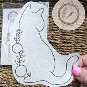May include: A white cat outline with a floral design on its back. The outline is on a white background and is ready for embroidery.