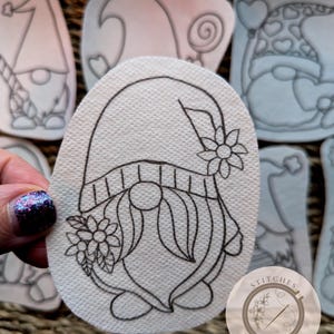 Puede incluir: Un dibujo en blanco y negro de un gnomo con una flor en su sombrero. El gnomo lleva un sombrero con una banda a rayas y tiene una barba larga. El dibujo está sobre un fondo blanco.