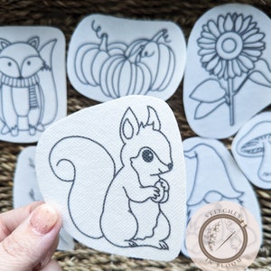 May include: A set of iron-on patches featuring various fall-themed designs, including a squirrel, a fox, pumpkins, a sunflower, a mushroom, and a gnome. The patches are white with black outlines and are ready to be ironed onto fabric.