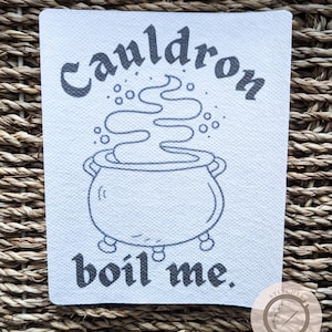 Puede incluir: Un parche de lona blanco con texto negro y un dibujo de línea negra de un caldero con vapor saliendo de él. El texto dice "Cauldron boil me."