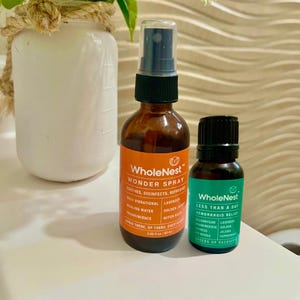 May include: Two brown glass bottles with black caps and orange and green labels. The larger bottle is labelled "WholeNest Wonder Spray" and the smaller bottle is labelled "WholeNest Less Than A Day Hemorrhoid Relief".