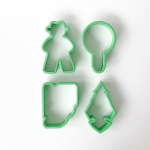 May include: Set of four green plastic cookie cutters, shaped like a person, a lightbulb, a tree, and a letter W.