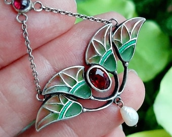 May include: A silver pendant necklace with a green and pink enamel design featuring three leaves and a red gemstone. A single pearl dangles from the bottom of the pendant.