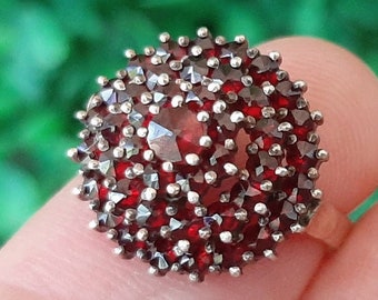 Puede incluir: Un anillo de plata con un grupo de piedras de granate rojo engastadas en un diseño circular.