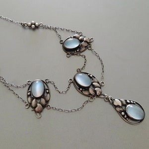 Puede incluir: Un collar de plata con una cadena delicada y cuatro colgantes ovalados de piedra lunar. Cada colgante est&aacute; engastado en un marco de plata con un dise&ntilde;o floral.