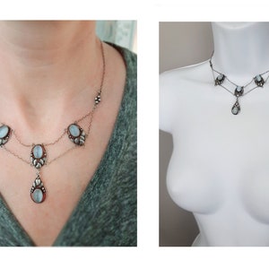 Puede incluir: Un collar de plata con un colgante en forma de l&aacute;grima y piedras ovaladas. El collar tiene dos cadenas y est&aacute; adornado con peque&ntilde;as cuentas.
