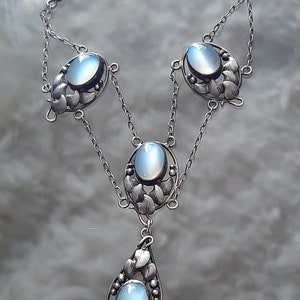 Puede incluir: Un collar de plata con una cadena delicada y cuatro colgantes ovalados de piedra lunar. Cada colgante est&aacute; rodeado de un dise&ntilde;o floral.