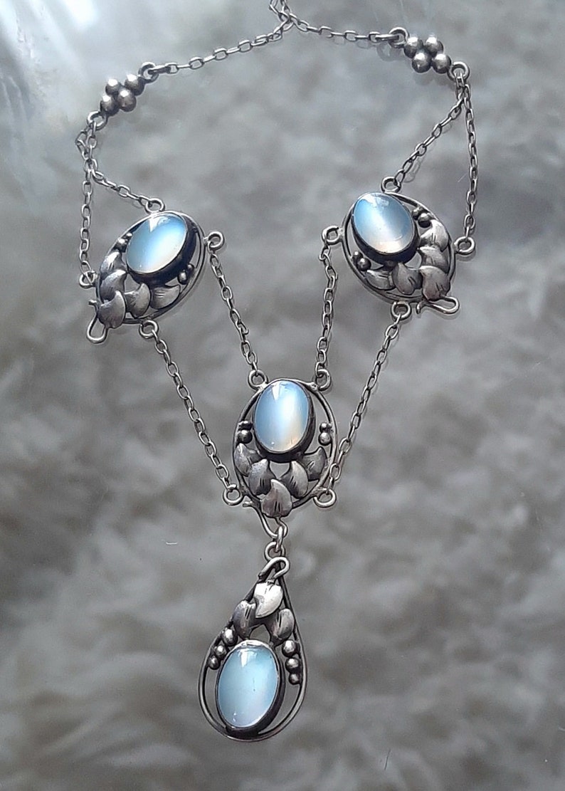 Puede incluir: Un collar de plata con una cadena delicada y cuatro colgantes ovalados de piedra lunar. Cada colgante est&aacute; rodeado de un dise&ntilde;o floral.