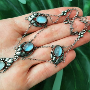 Puede incluir: Un collar de plata con un colgante en forma de l&aacute;grima con una piedra de luna azul. El collar tiene tres acentos ovalados de piedra de luna y una cadena delicada.