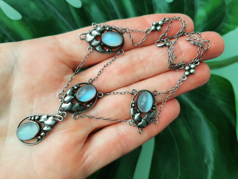 Puede incluir: Un collar de plata con un colgante en forma de l&aacute;grima con una piedra de luna azul. El collar tiene tres acentos ovalados de piedra de luna y una cadena delicada.