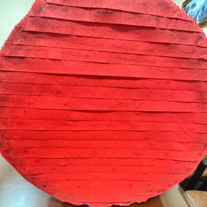 Puede incluir: Una pi&ntilde;ata grande, redonda y roja, construida con papel crep&eacute; en capas. La pi&ntilde;ata est&aacute; suspendida por una cuerda blanca, lista para una fiesta. Los bordes de la pi&ntilde;ata est&aacute;n ligeramente deshilachados.