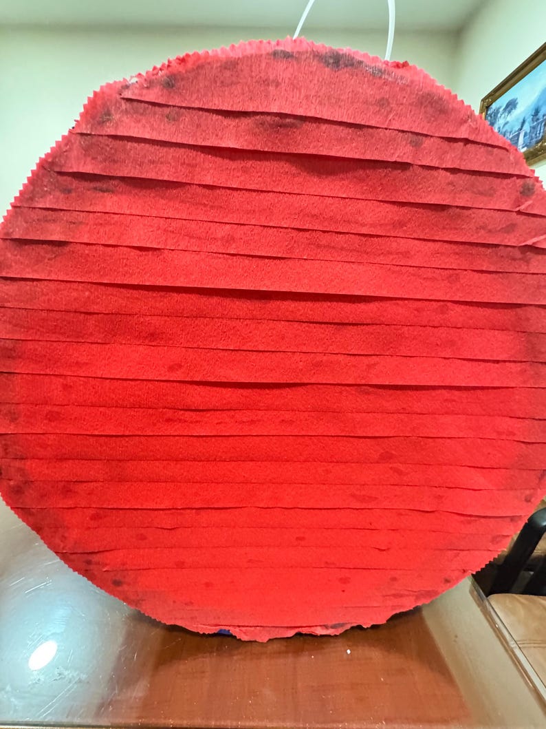 Puede incluir: Una pi&ntilde;ata grande, redonda y roja, construida con papel crep&eacute; en capas. La pi&ntilde;ata est&aacute; suspendida por una cuerda blanca, lista para una fiesta. Los bordes de la pi&ntilde;ata est&aacute;n ligeramente deshilachados.
