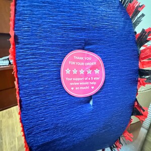 Puede incluir: Decoraci&oacute;n de papel crep&eacute; azul con flecos rojos y negros. Una pegatina rosa dice "GRACIAS POR SU PEDIDO" y solicita una rese&ntilde;a de 5 estrellas. El art&iacute;culo es probablemente para una fiesta.