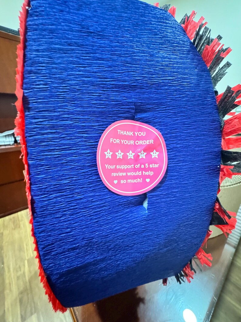 Puede incluir: Decoraci&oacute;n de papel crep&eacute; azul con flecos rojos y negros. Una pegatina rosa dice "GRACIAS POR SU PEDIDO" y solicita una rese&ntilde;a de 5 estrellas. El art&iacute;culo es probablemente para una fiesta.