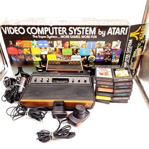 May include: An Atari Video Computer System console with controllers and game cartridges. The console is black and brown with the Atari logo. The box features game screenshots and the text "VIDEO COMPUTER SYSTEM by ATARI".