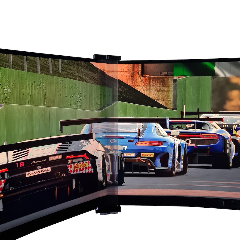 May include: A curved monitor displays a racing game with several race cars. The cars are various colors, including black, blue, and red. The game appears to be set on a racetrack with green barriers.