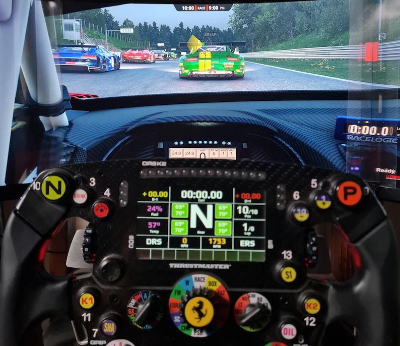 May include: A close-up of a racing simulator setup featuring a Thrustmaster steering wheel with multiple buttons and a digital display showing race data. The screen displays a racing game with cars on a track.
