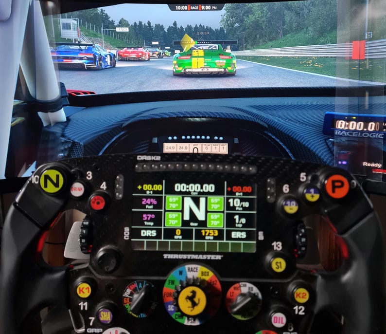 May include: A close-up of a racing simulator setup. A black steering wheel with multiple buttons and a digital display is in focus. The screen shows a race track with several cars. The wheel has the Ferrari logo.