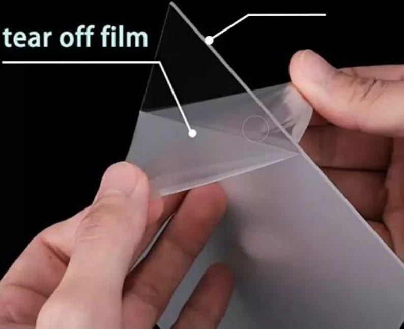 May include: Close-up of a person peeling a clear, protective film from a surface. The text "tear off film" is visible in the upper left corner. The film is being peeled back to reveal the surface underneath.