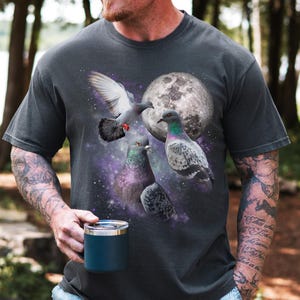 May include: Dark gray t-shirt featuring a graphic of several pigeons with a full moon and a starry background. The shirt has a vintage, washed look. The word "PEPPER" is printed in white on the bottom right.