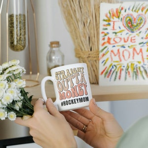 Hockey Mom 11oz Ceramic mug with graphic that says straight outta money, at the bottom it says hockey mom. This makes perfect hockey mom gifts for mothers day and a birthday, or to show your appreciation for your hockey mom, hockey coach or manager