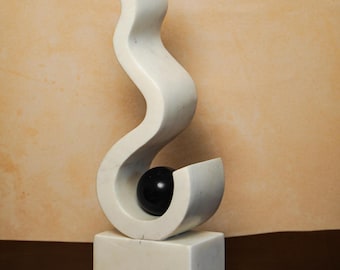 Puede incluir: Escultura de mármol blanco con un diseño curvo y fluido. Una esfera negra está acunada dentro de las curvas de la escultura. La escultura descansa sobre una base rectangular, mostrando una obra de arte abstracta moderna.