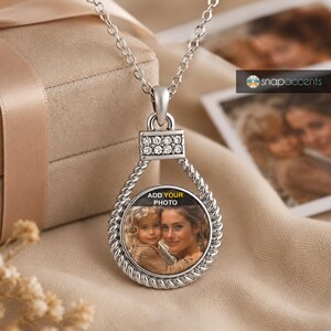 May include: A silver-toned pendant necklace featuring a circular frame with a twisted rope texture. The top connector is embellished with small clear crystals. The center holds a circular insert displaying a photograph of a child and an adult.